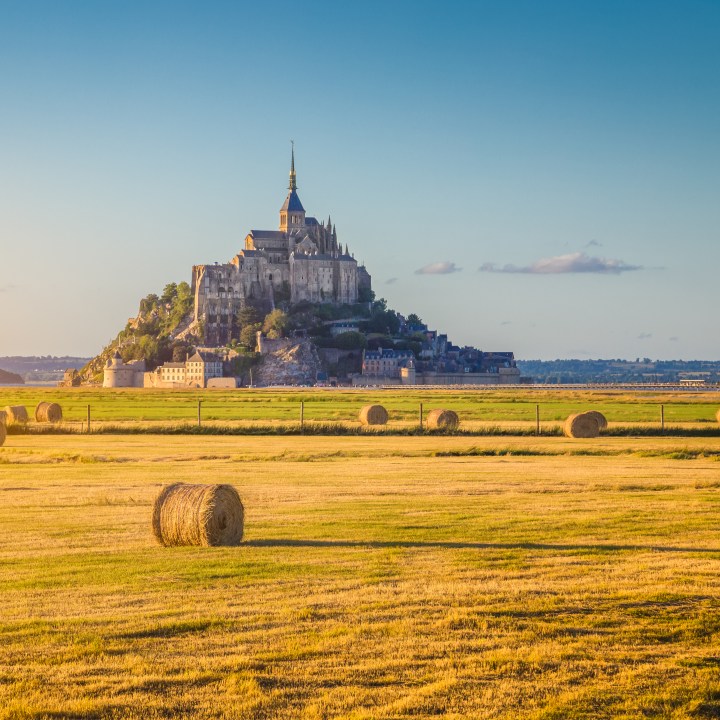 Beautiful view of famous historic Le Mont Saint-Michel in golden evening light at sunset in summer with hay bales on fields with retro vintage Instagram style pastel filter effect, Normandy, France