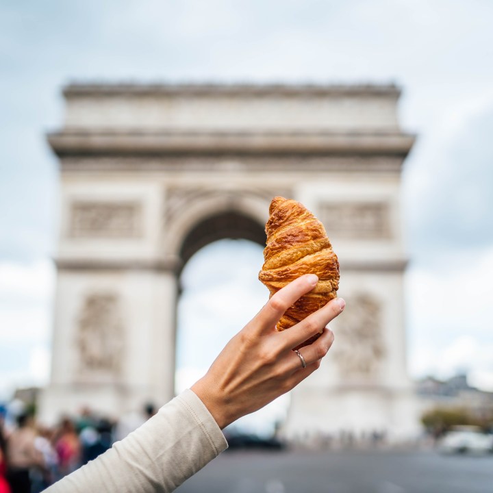 Woman's hand holding croissant in front of the famous Arc de Triomphe, (Arch of Triumph) in Paris, France